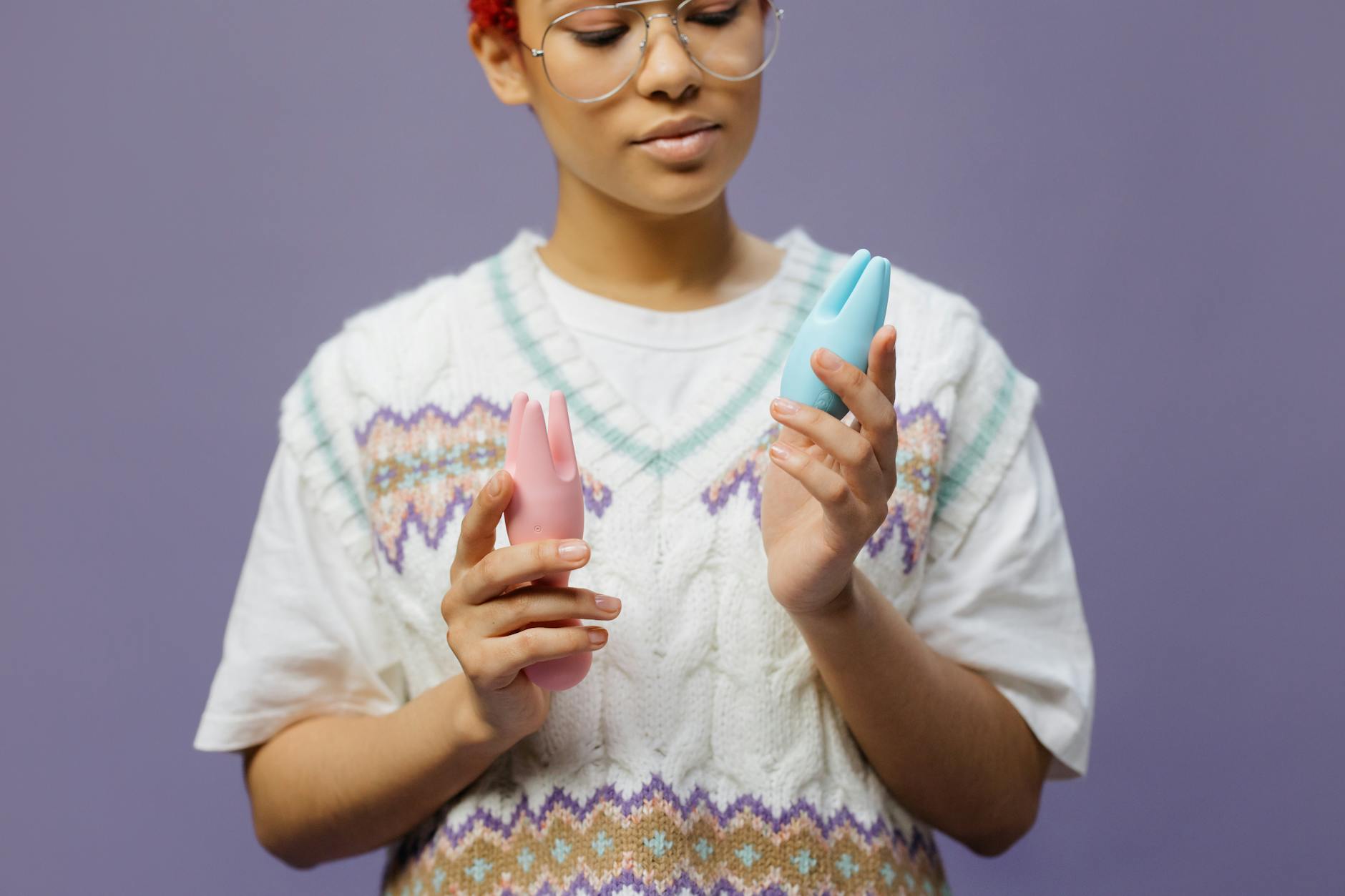 Woman thoughtfully holding a blue and pink silicone vibrator, exploring personal pleasure.